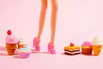 Plastic toy legs with high heels and little sweets on pastel pink background